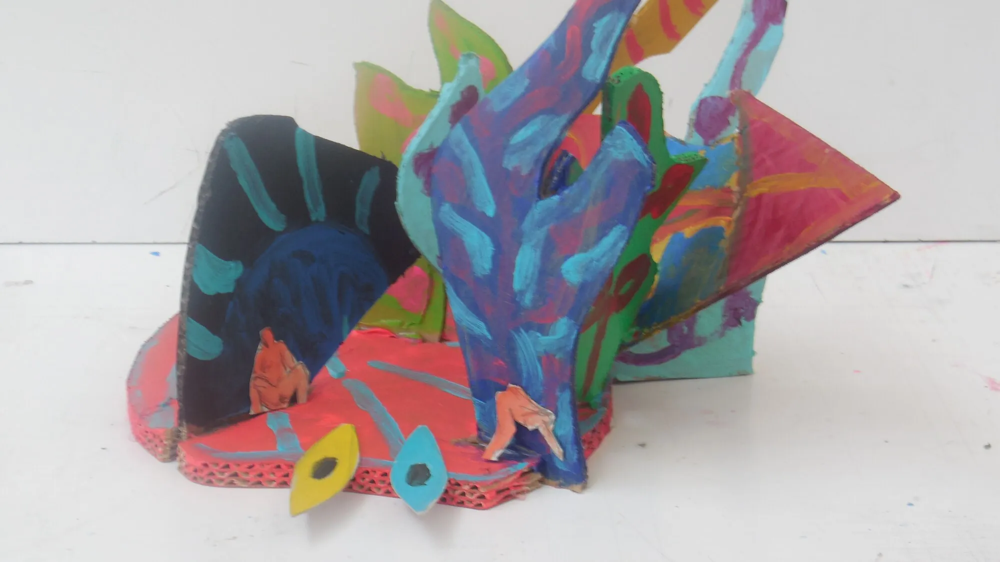 Sculpture en carton peint aux feuilles bleues, vertes et roses sur socle rose, petites figures collees, oeuvre de Marc Sardina