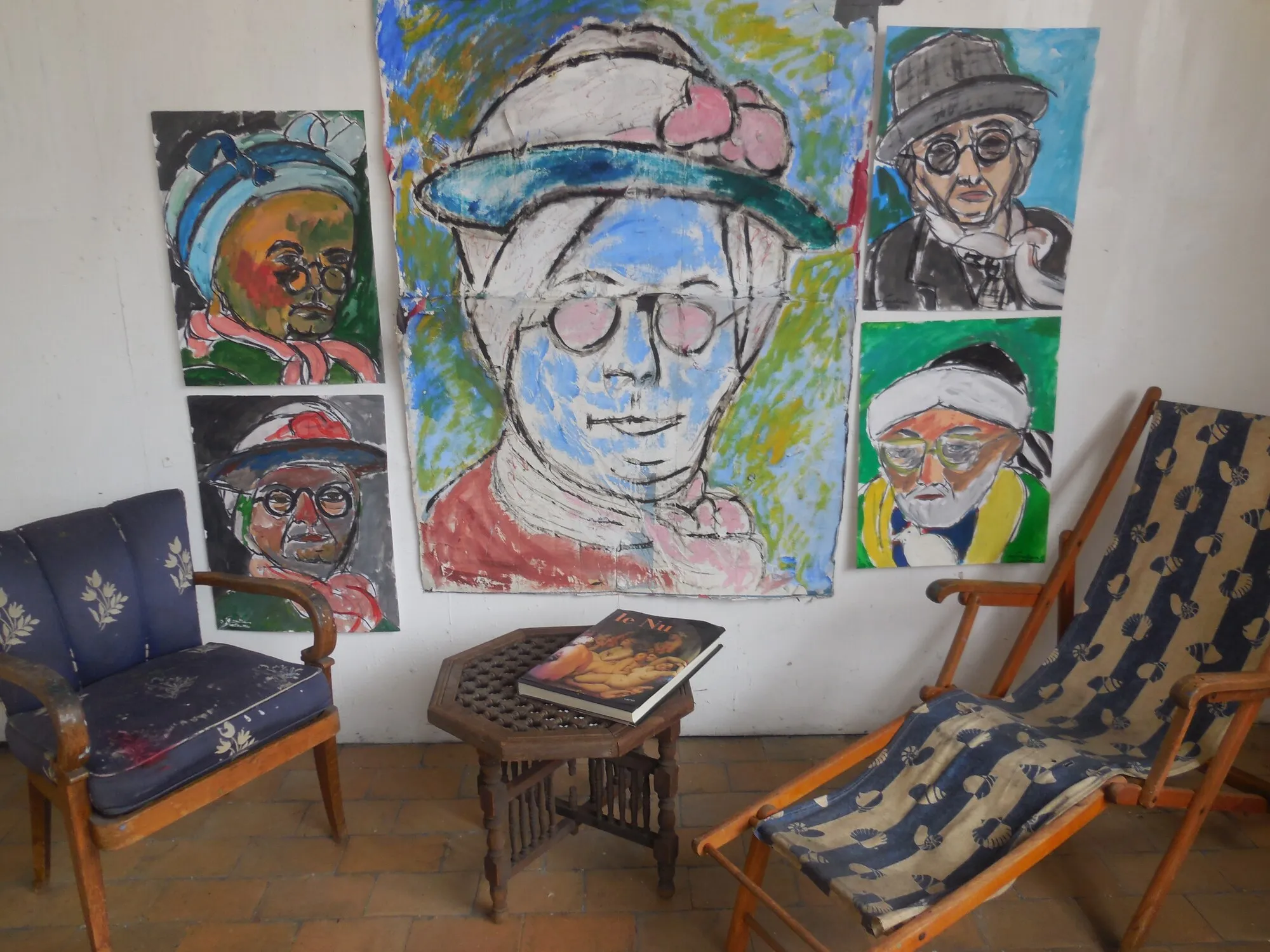 Cinq portraits d'hommes à chapeaux accrochés au mur d'un atelier, fauteuil et chaise longue, installation de Marc Sardina