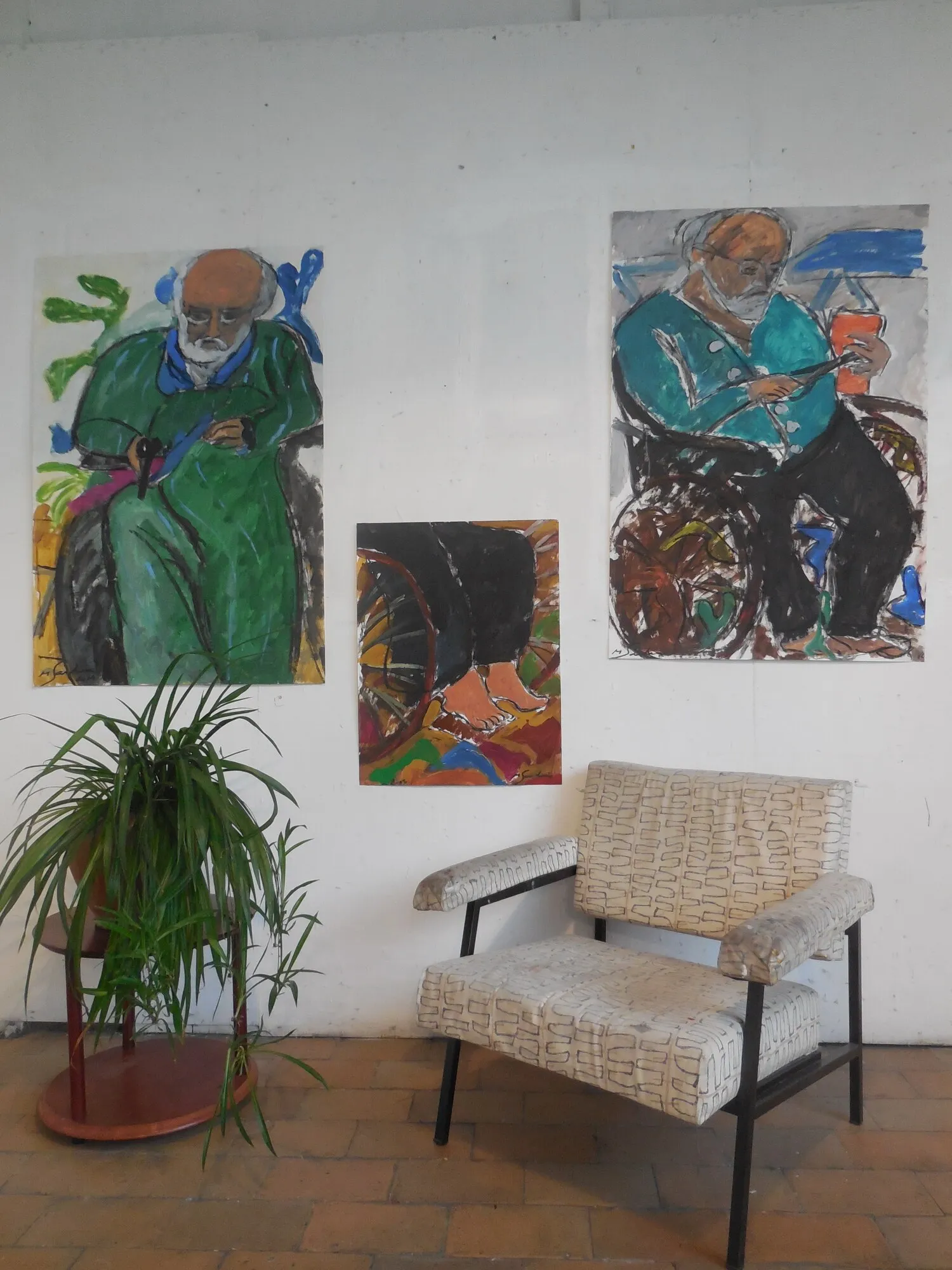 Trois portraits d'un vieil homme assis, vert et turquoise, au mur d'un atelier avec plante et fauteuil, installation de Marc Sardina