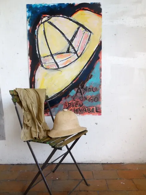 Casque colonial peint en jaune sur fond rouge et bleu, chaise avec vrai casque et veste kaki devant, installation de Marc Sardina